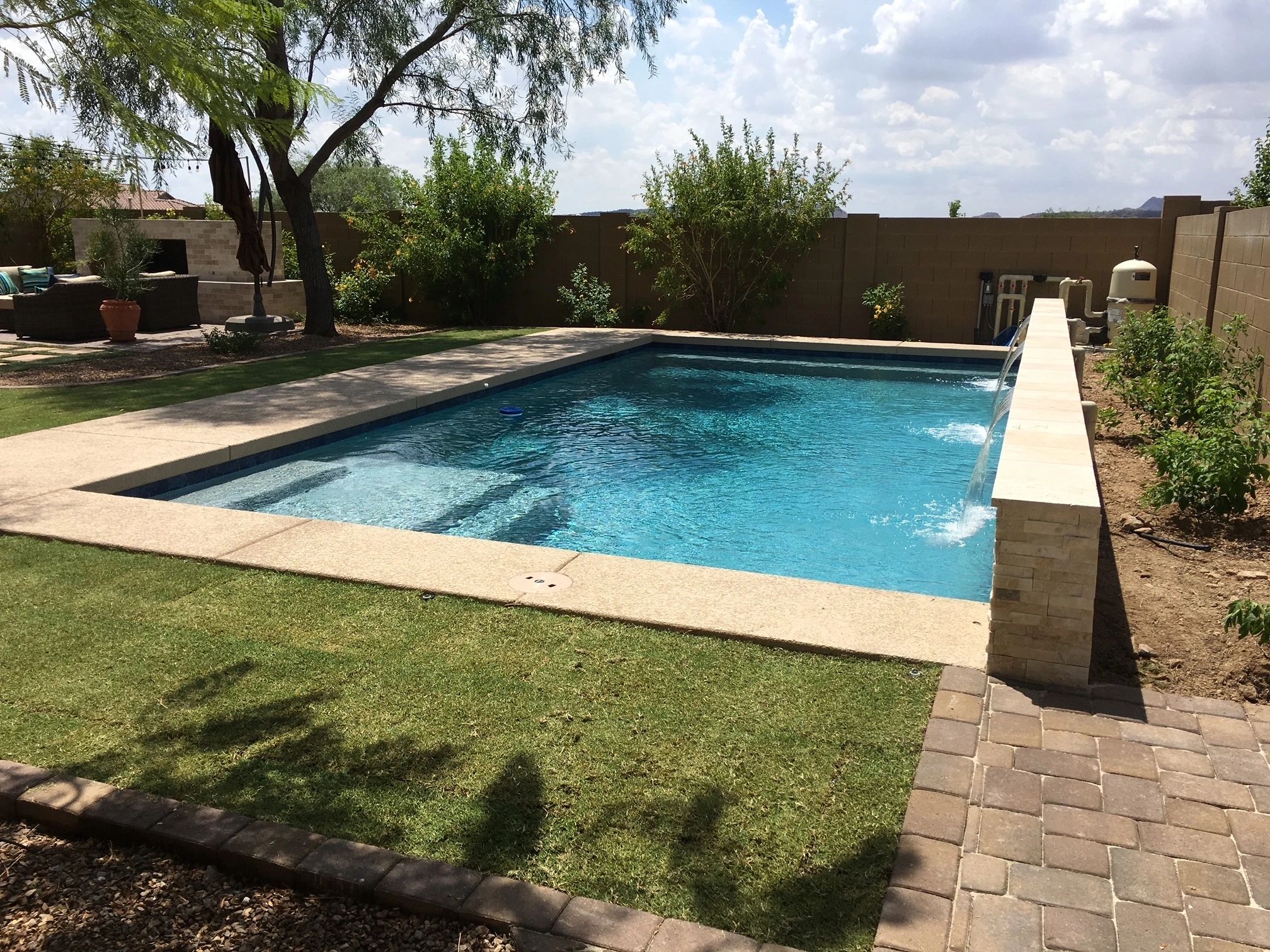 A pool with a stone wall and grass around it.