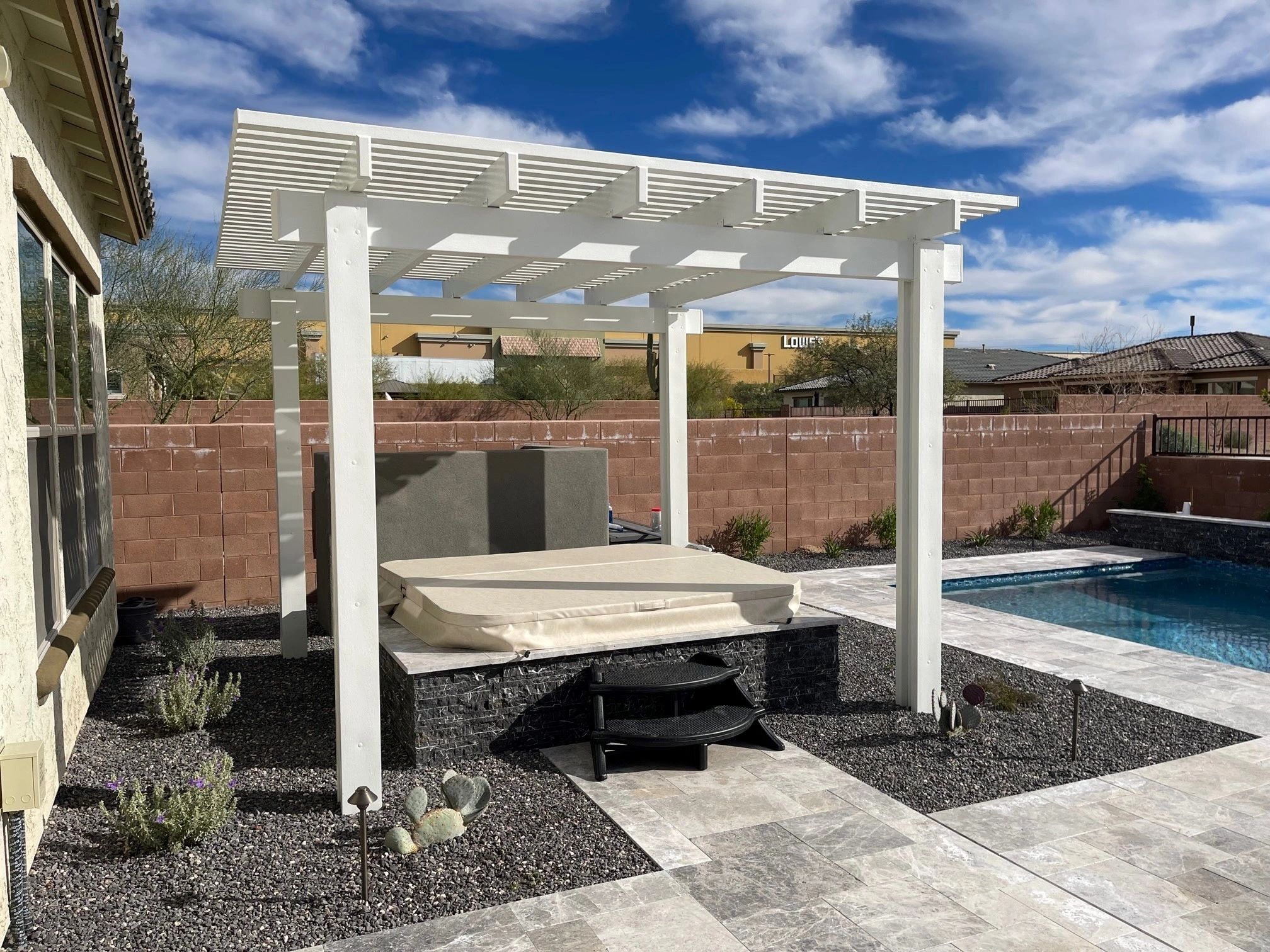 A white pergola with a bench in the middle of a backyard.