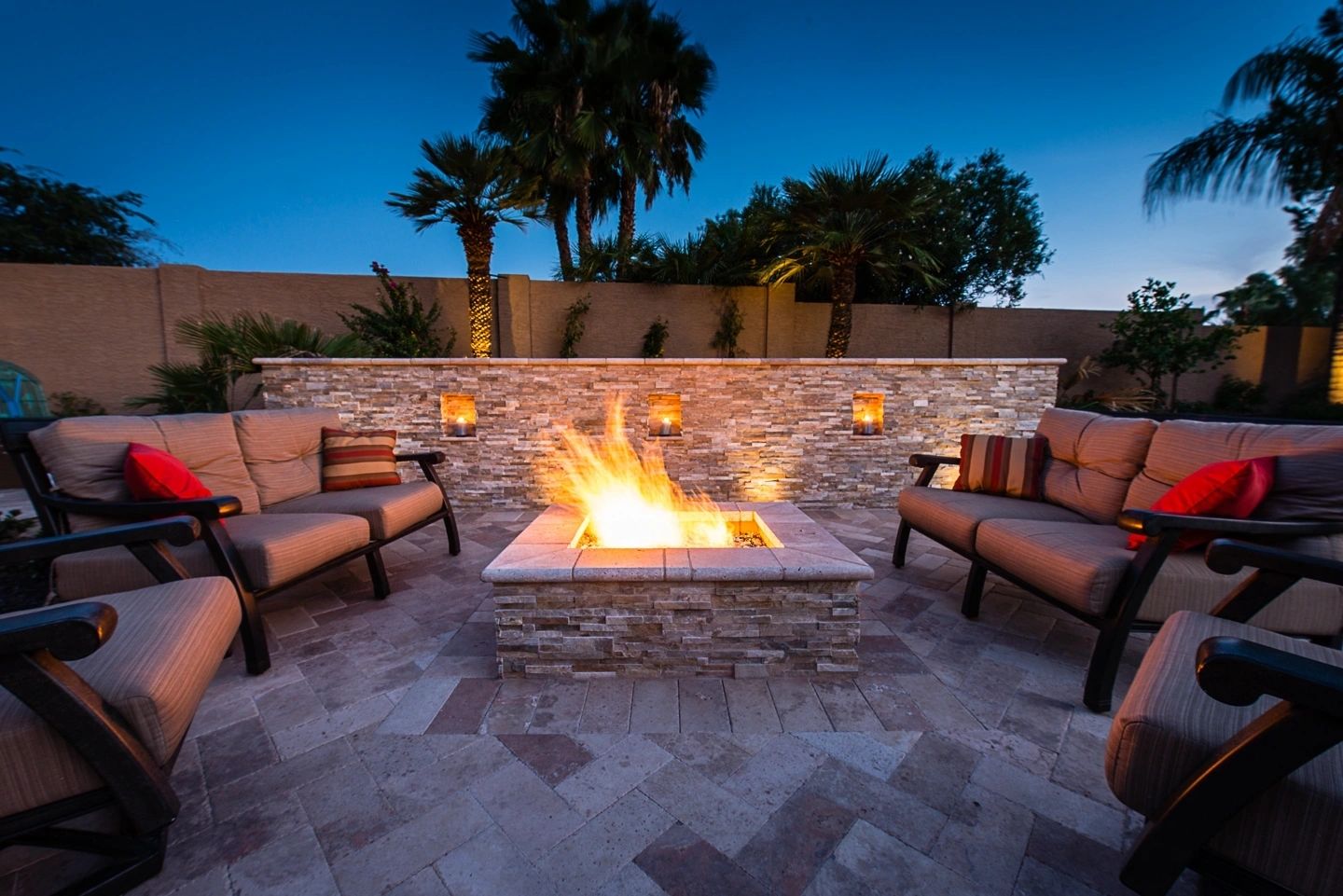 A fire pit with chairs around it and palm trees in the background.