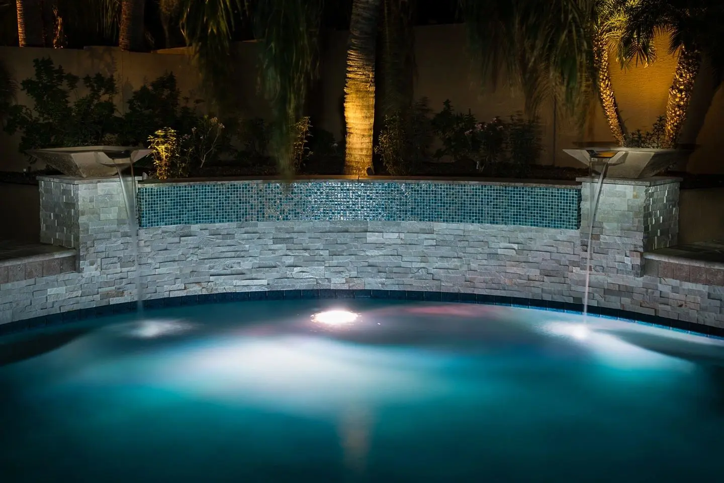 A pool with lights on and water coming out of the bottom.