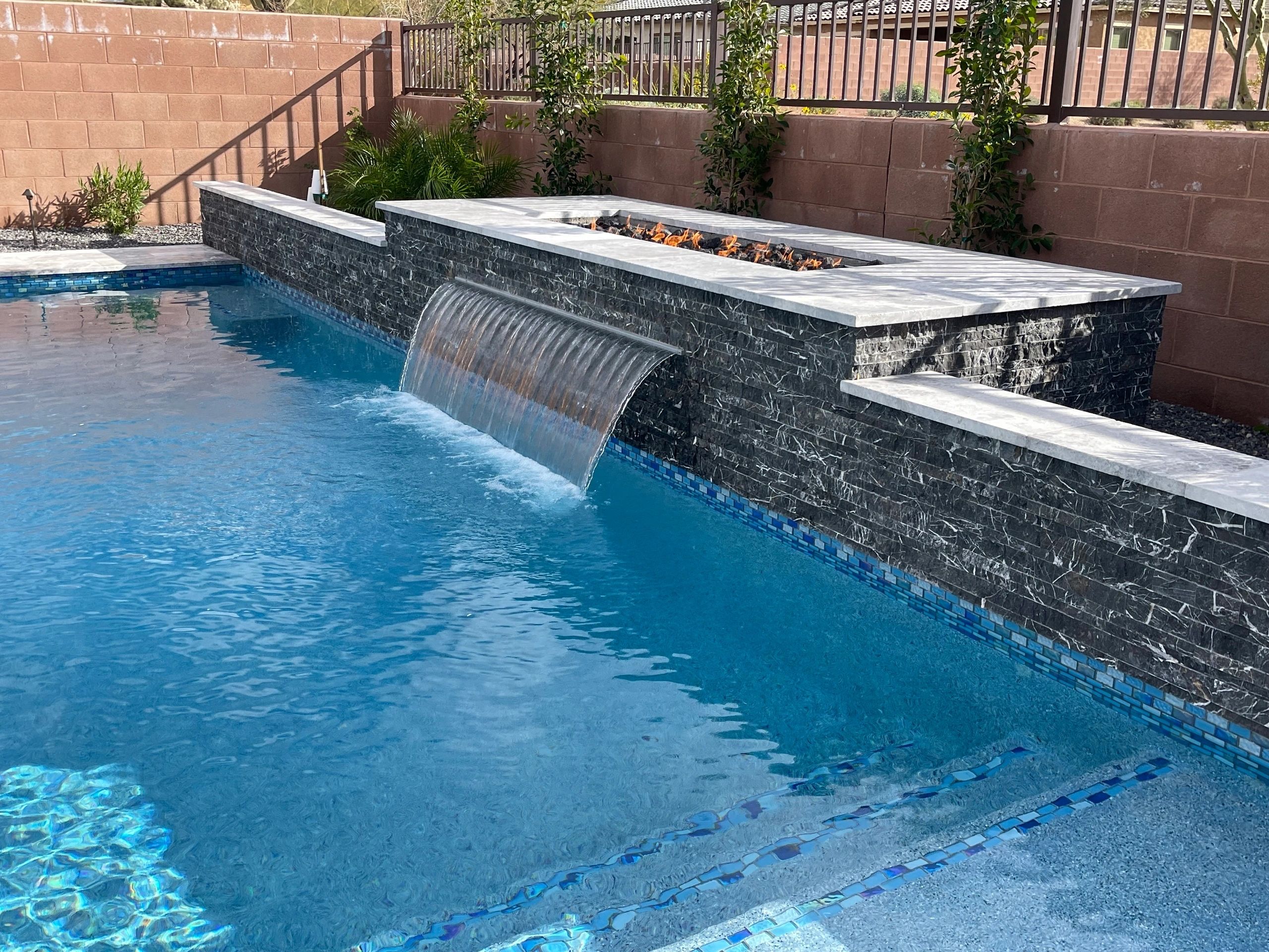 A pool with a waterfall and stone wall.